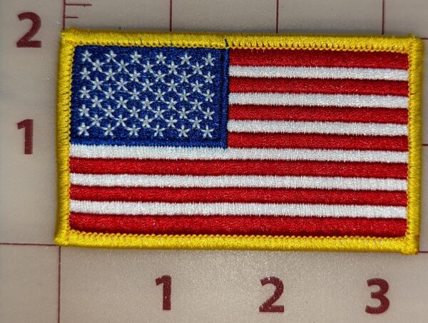 Close-up of TactiTether American flag patch with red, white, and blue colors, and a yellow border, placed on a measuring grid.